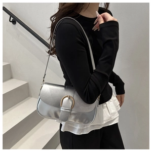 Détail du sac à bandoulière argenté métallisé avec boucle en D dorée sur fond blanc