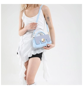 Detail of light blue crossbody bag featuring a round metal magnetic buckle and textured panel