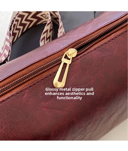 Detail der weinroten PU-Tasche mit poliertem Goldreißverschluss und Webriemen-Textur