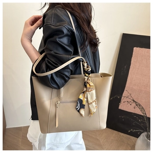 Close-up of a khaki tote bag with a decorative silk scarf on the handles and a zipper pocket