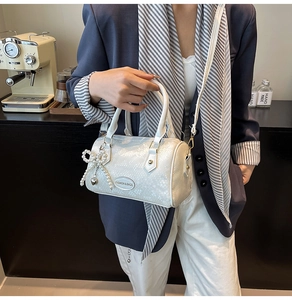 Détail du sac Boston blanc nacré avec pendentif en perles dans un décor de café