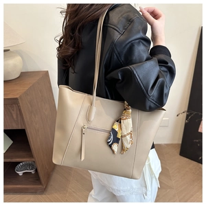 Detail of a beige leather tote bag featuring a side zipper pocket and elegant floral silk scarf