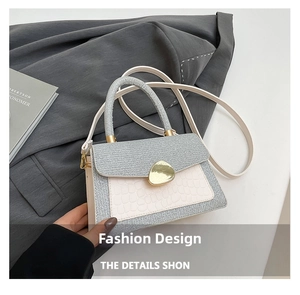 Detail der weißen Krokodil-Handtasche mit goldenem Drehverschluss auf grauem Blazer-Hintergrund