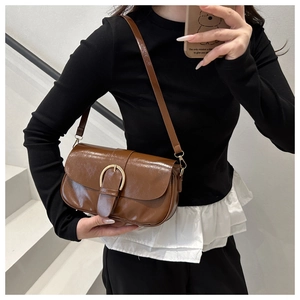 Détail d'un sac bandoulière marron brillant avec une grande boucle fer à cheval dorée