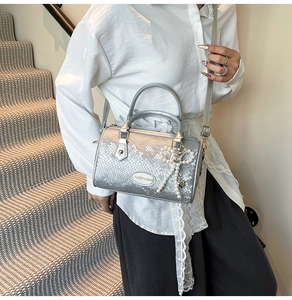 Silver snakeskin Boston bag with pearl bow charm shown in a lifestyle street setting