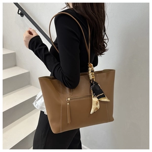 Brown leather tote bag with silk scarf detail and white stitching on a model
