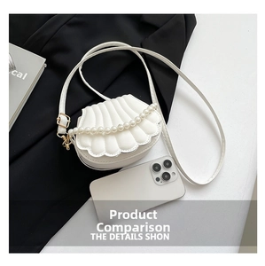 Detail of white shell-shaped mini bag with pearls and golden hardware next to phone