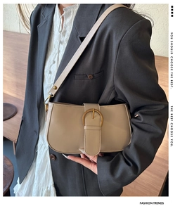 Détail du sac sous le bras en cuir beige avec boucle dorée ronde sur le mannequin