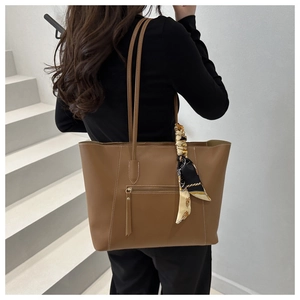Close-up of brown PU leather tote bag with silk scarf and decorative tassel on strap