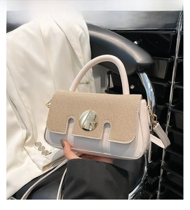 Detail of beige crossbody bag featuring straw weave flap and large gold metal buckle
