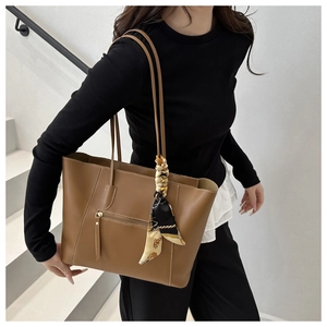 Detail of brown leather tote bag featuring a decorative silk scarf and front zipper pocket