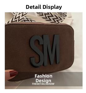 Macro shot of dark brown suede bag featuring large black SM logo and wavy strap detail