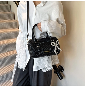Detail of black Boston bag with snake texture and elegant pearl bow charm accessory