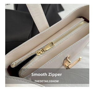 Close-up of smooth gold zipper and burgundy lining on a minimalist cream leather handbag