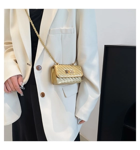 Close-up of golden mini chain bag with quilted patterns and metal twist lock on white blazer