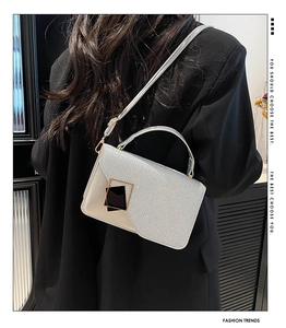 Detailed view of silver textured crossbody bag with gold hardware worn by a model