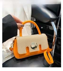 Close-up of orange leather crossbody bag with beige woven flap and round metal lock