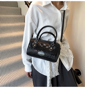 Detail of black Boston bag with snakeskin texture, gold hardware and fashion emblem