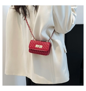 Detail of red quilted mini crossbody bag with golden chain strap on a white blazer