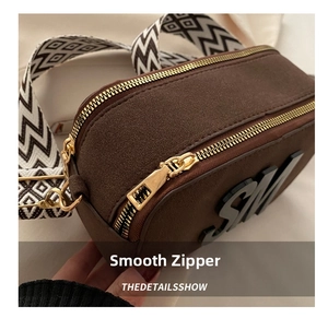 Detail showing smooth gold metal zipper and frosted brown leather texture of the bag