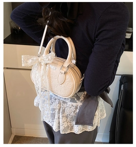 Detail of cream crossbody bag featuring embossed love songs text and lace bow detail