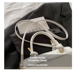 Detail view of white handbag featuring knot handle design and gold metal rings