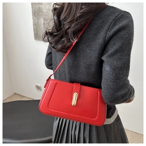 Détail d'un sac à bandoulière rouge avec fermoir doré sur fond de pull gris texturé