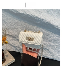 Detail of white quilted mini crossbody bag with gold rectangular clasp and chain strap