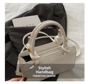 Detailed view of white handbag with unique knot handle and gold hardware rings