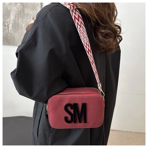 Détail du sac bandoulière bordeaux avec logo SM 3D et large sangle géométrique