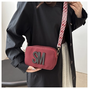 Gros plan du sac en toile bordeaux avec décor de lettres SM et bandoulière à motifs