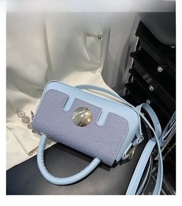 Detail of light blue textured handbag with large gold circular buckle and slim shoulder strap