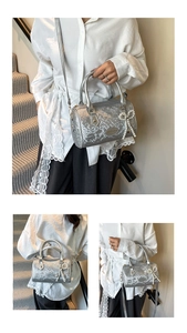 Close-up of silver snake-embossed Boston bag with pearl bow charm and metal logo
