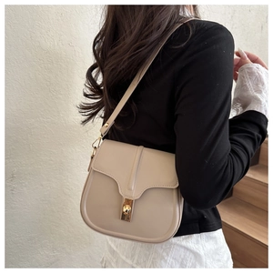 Close-up of a beige saddle bag with gold metal buckle on female shoulder in bright setting