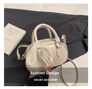 Detail of cream Boston bag featuring embossed patterns and a delicate lace bow accent