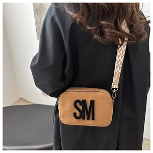 Détail d'un sac bandoulière en daim avec bandoulière large et logo SM brodé