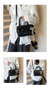 Detail of black faux snakeskin boston bag featuring pearl bow charm and shoulder strap