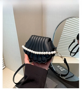 Detail of black shell-shaped mini bag with pleated texture and pearl handle
