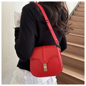 Detail of red saddle bag with gold metal clasp worn over a black and white outfit