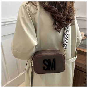 Brown textured camera bag with wide patterned strap and SM logo shown on a model