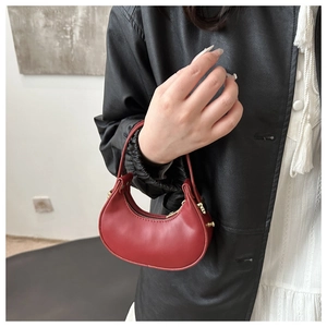 Dettaglio di una mini borsa a mezzaluna rossa con finiture dorate tenuta da un modello