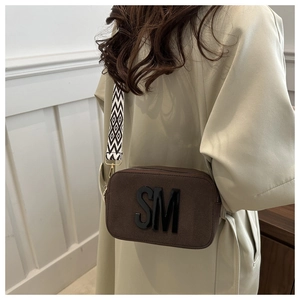 Detail of dark brown crossbody camera bag with wide geometric strap on beige coat