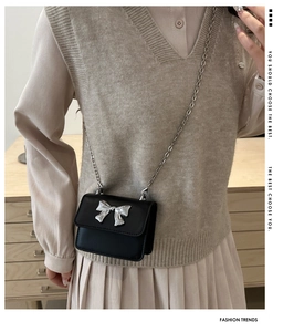 Detailed view of mini black crossbody bag with silver bow ornament on a model
