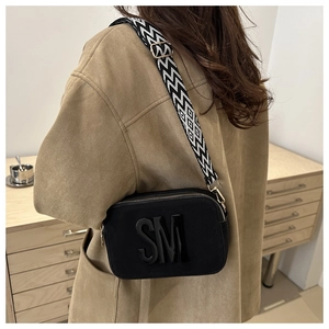 Détail du sac caméra en cuir noir avec bandoulière géométrique et logo en relief