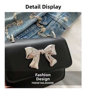 Close-up of black mini crossbody bag with a large silver metal bow buckle on denim