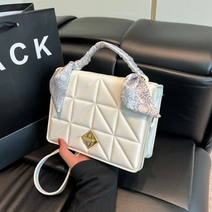 Sac à main blanc matelassé avec fermoir doré et foulard sur un canapé noir