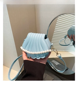 Detailed view of light blue shell crossbody bag with vertical quilting and pearl handle