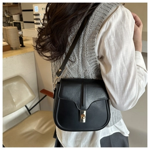 Detail shot of a black leather saddle bag with a golden twist lock on a minimalist model