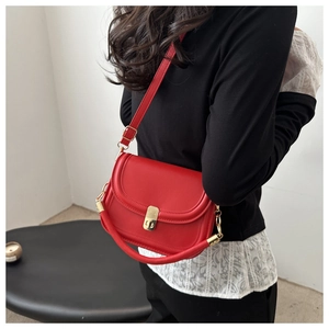 Detail of red leather crossbody bag featuring gold buckle closure and sleek curved base