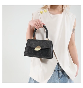 Close-up of black glitter handbag featuring crocodile pattern and gold metal buckle